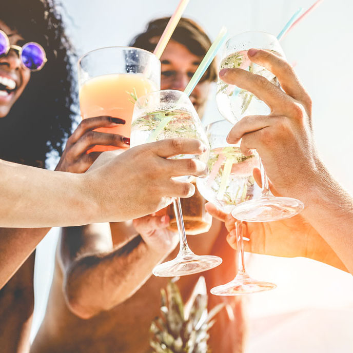 Group of happy friends cheering with tropical cocktails at boat party - Young people having fun in caribbean sea tour - Youth and summer vacation concept - Focus on bottom hands glass