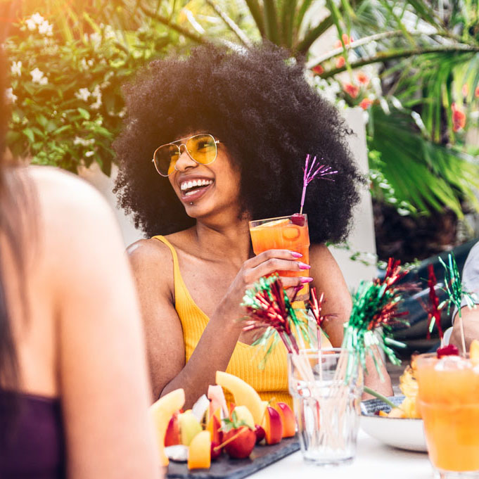Happy black beautiful woman having fun drinking cocktail with friends outdoor. Group of millennials laughing together at a party