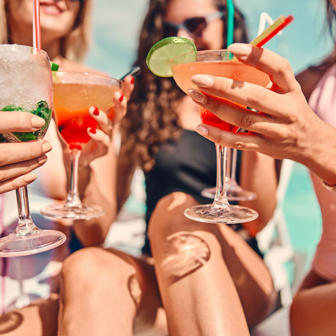 Women clinking glasses with cocktails at poolside. Close up view. Selective focus