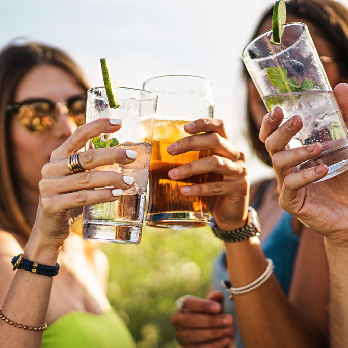 Cheerful group of millennial friends toasting alcoholic cocktails in the summer - people gathering cheering and drinking alcoholic drinks lifestyle concept